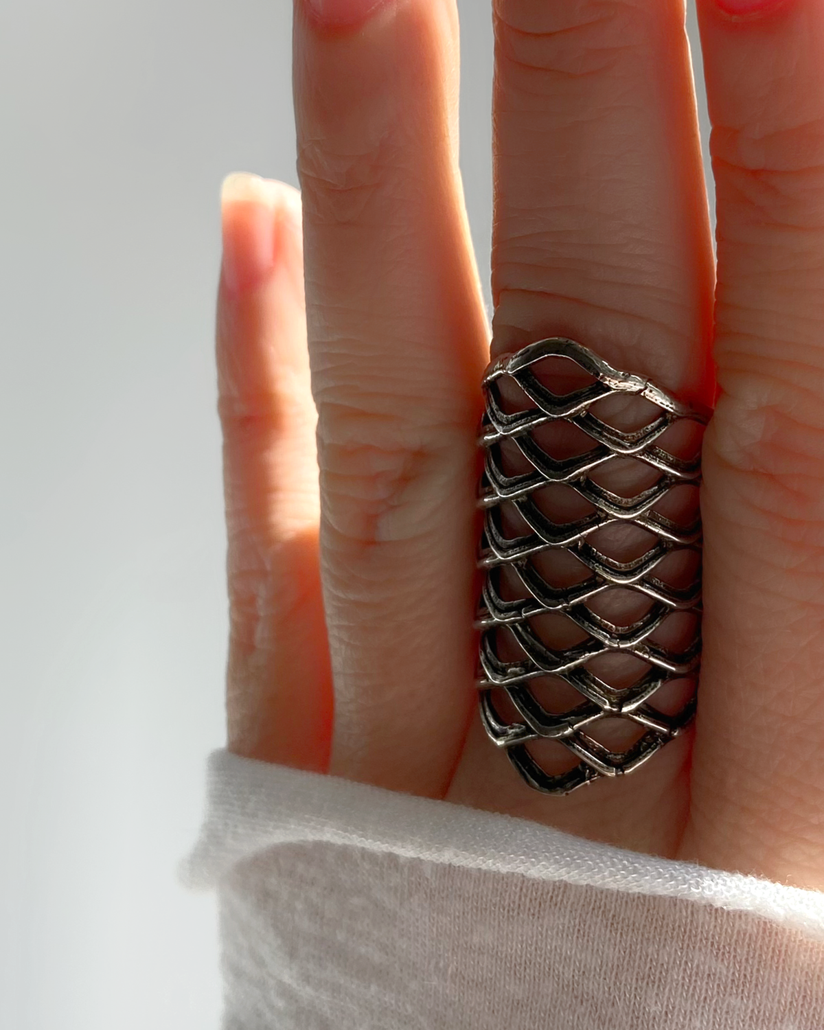 Bague large HELLES en laiton argenté patiné avec motif résille ajouré, portée sur un doigt, taille ajustable.