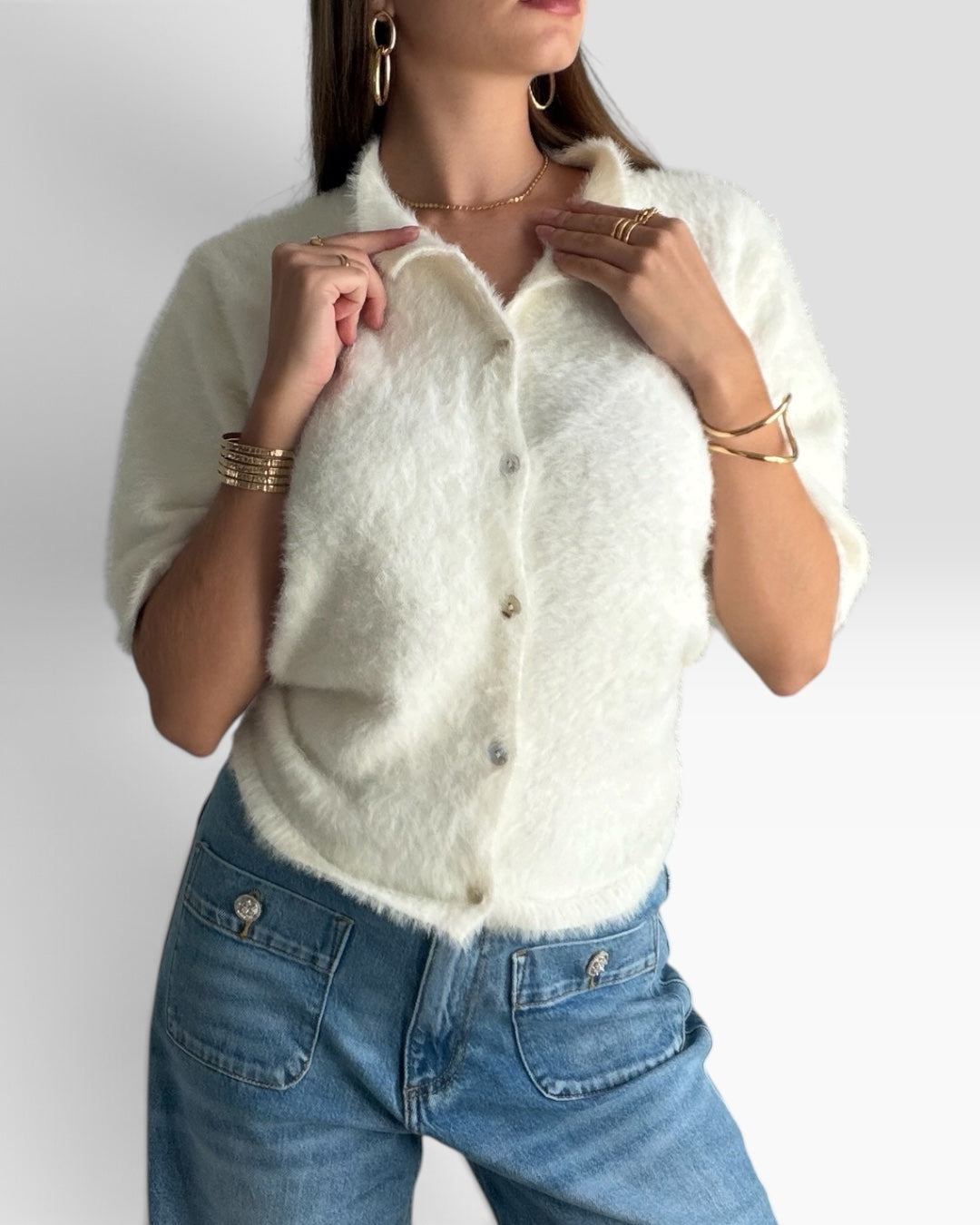 Gilet Nuage HELLES blanc à texture duveteuse, manches courtes et fermeture boutonnée, porté avec un jean bleu.