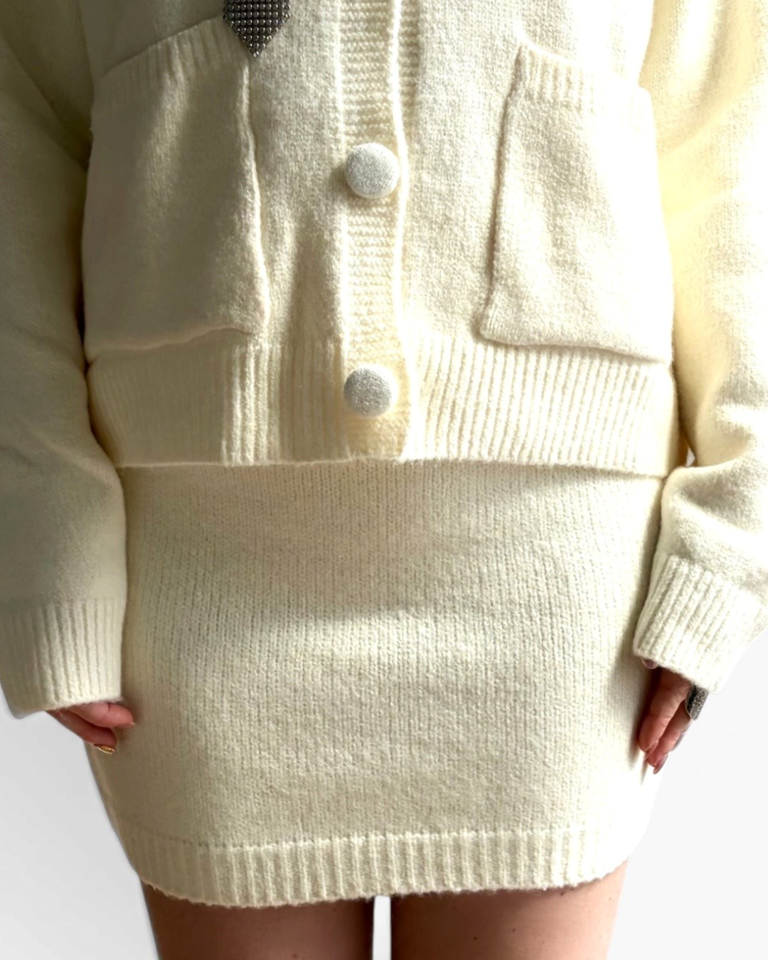 Jupe courte en maille HELLES couleur crème, douce et stretch, portée avec un gilet assorti pour un look cosy.