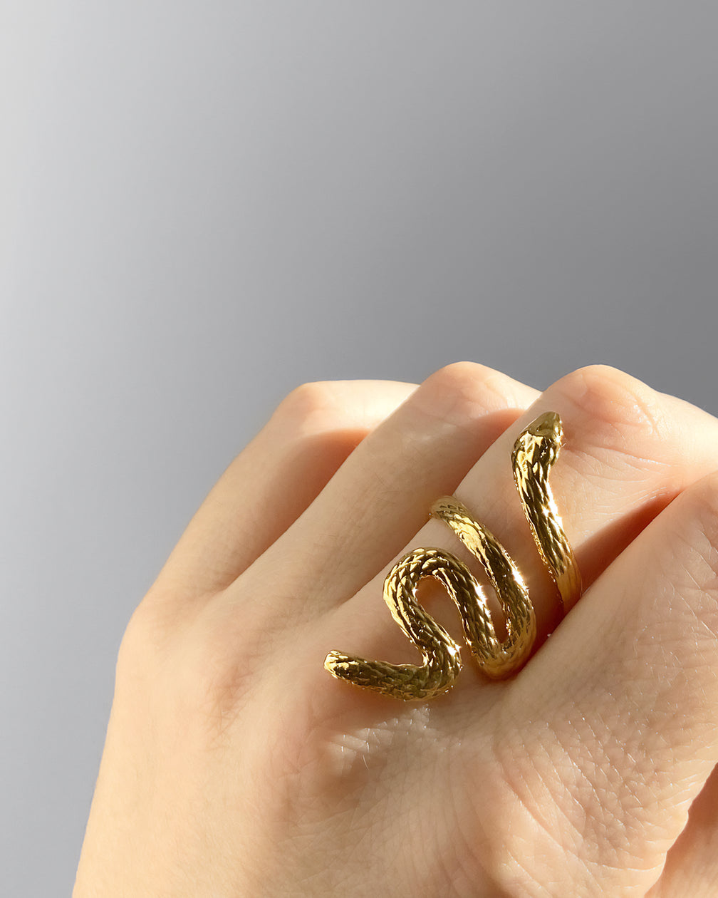 Bague HELLES Boa ajustable en forme de serpent en laiton doré à l'or fin 24 carats portée sur un doigt