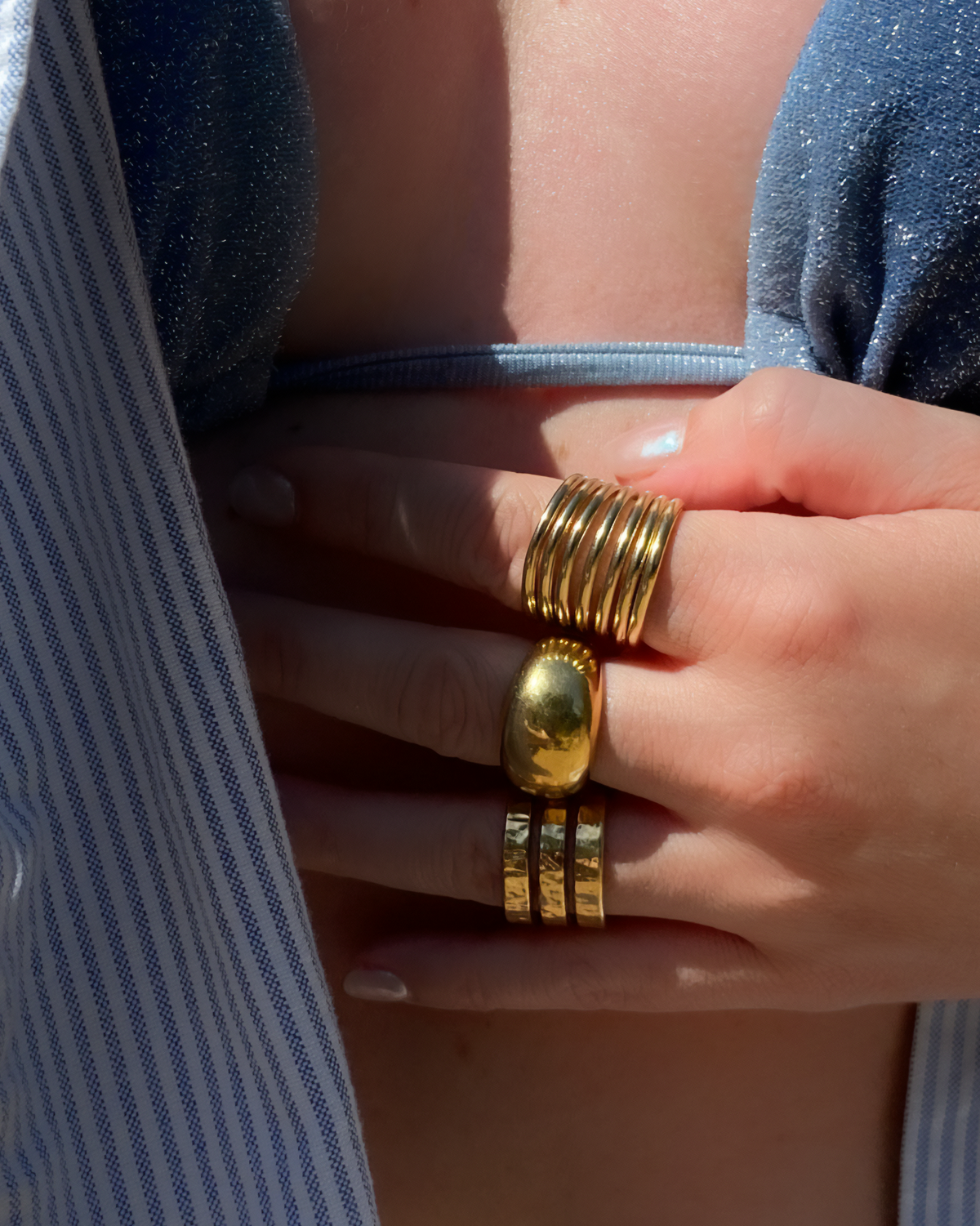 Bague Bombay HELLES ajustable en étain doré à l'or fin 24 carats, portée au doigt avec d'autres anneaux dorés.