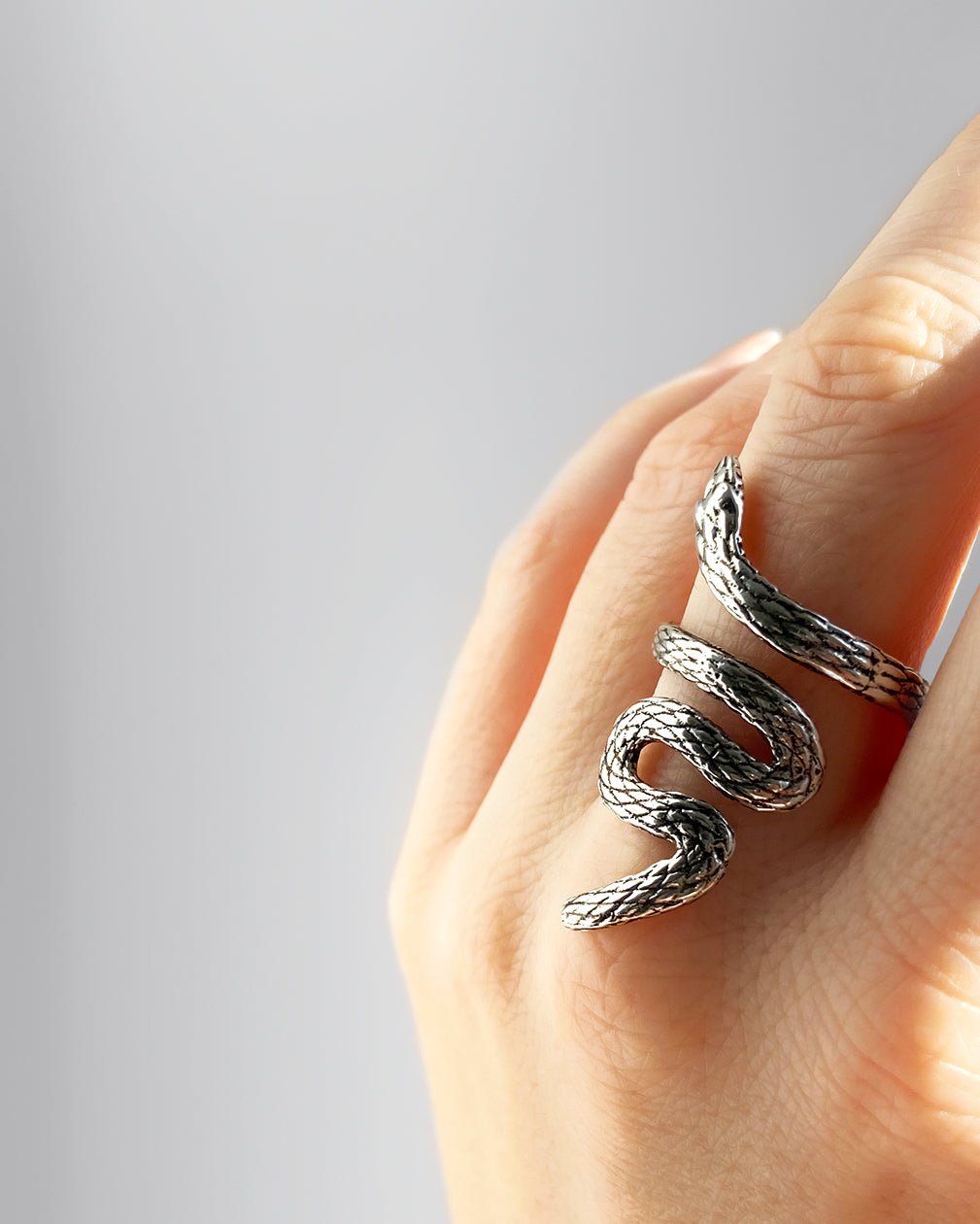 Bague serpent ajustable HELLES en laiton argenté patiné portée sur un doigt, design texturé de 4 cm de hauteur.