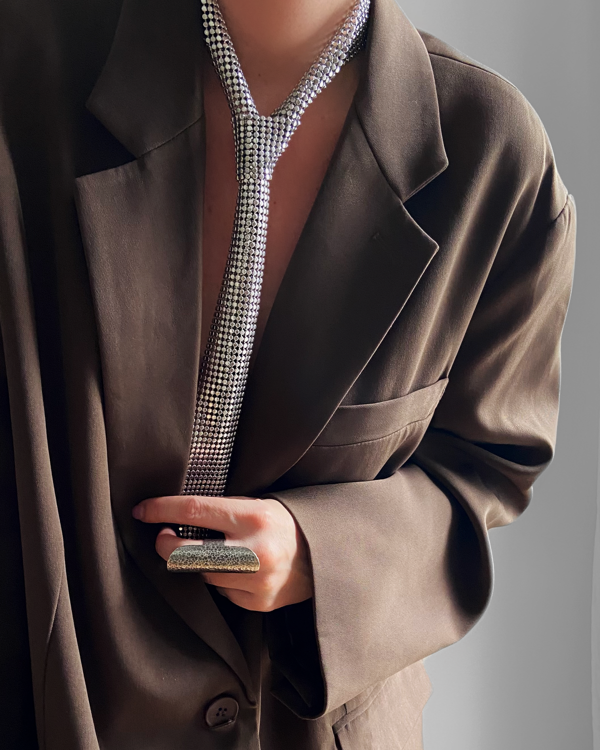 Cravate Bossy HELLES en laiton plaqué argent patiné, portée avec un blazer marron, style élégant et moderne